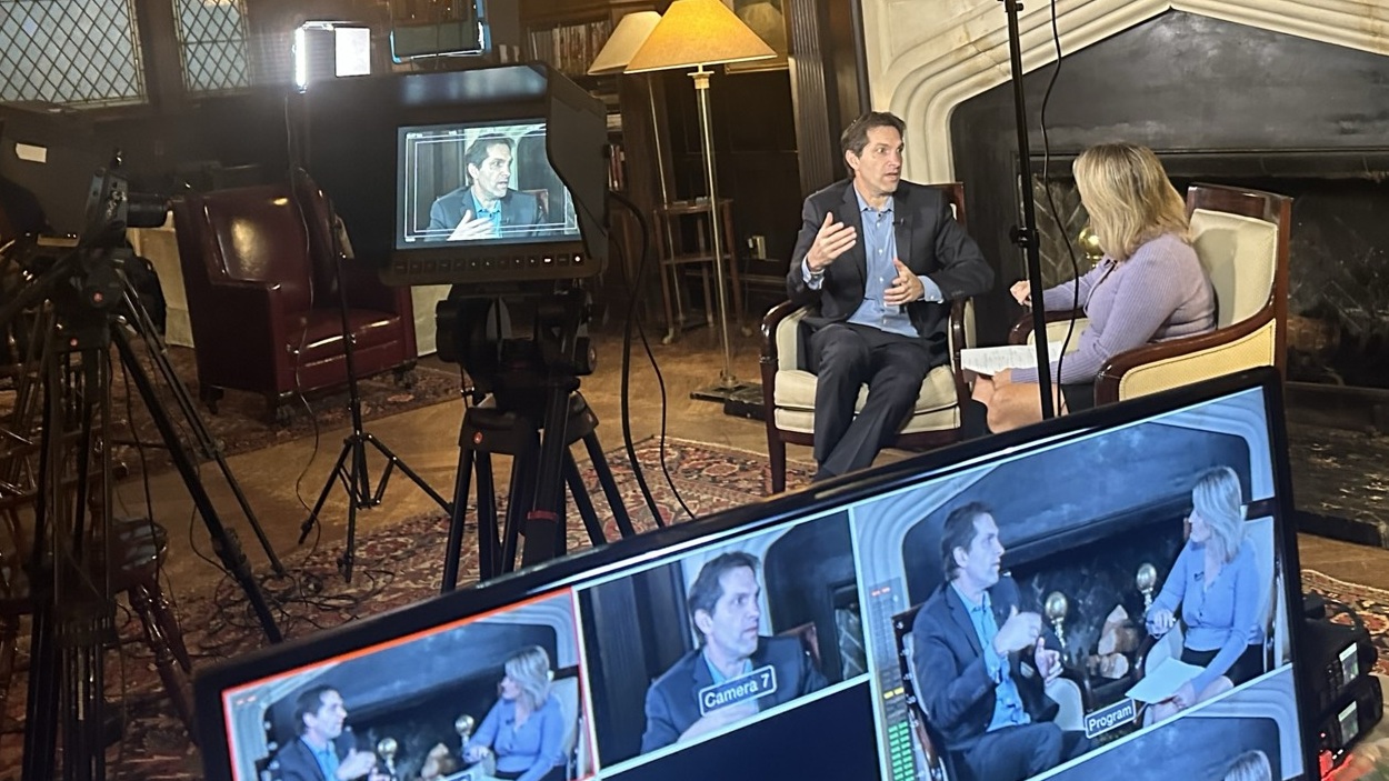On-location interview beside an ornate fireplace, with cameras and live editing monitors